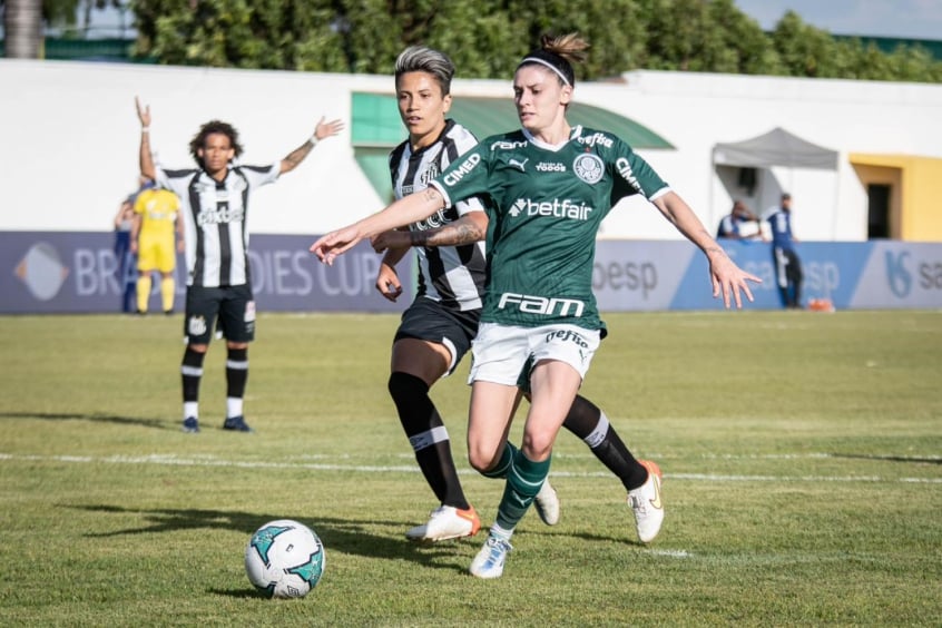 Santos x Palmeiras: Bruna Caldeiran, de braços abertos e fita no cabelo, com uniforme verde do Palmeiras, domina bola em partida contra o Santos. 