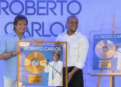 Em sua turnê pelo exterior, em 2019, o cantor Roberto Carlos teve o que comemorar e... ao lado de um astro do esporte. Em evento em Madri, o ex-lateral ROBERTO CARLOS entregou ao xará dois discos emblemáticos. Em um deles, a gravadora Sony Music celebrou a venda de 5 milhões de discos do cantor RC na Espanha. No outro, os mais de 140 milhões de discos comercializados por toda a América Latina. 