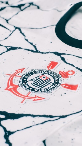 Detalhe do símbolo do clube no lado esquerdo do peito em meio às linhas imperfeitas em preto.