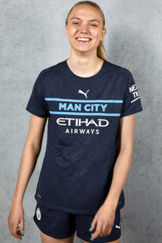 A terceira camisa do Manchester City ganhou um tom azul escuro e o tradicional azul celeste preenche o nome do clube. A zagueira dos Citizens, Esme Morgan, é a modelo da imagem.