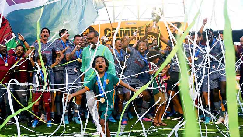 Jogadores levantam a taça, com os filhos no meio da festa.