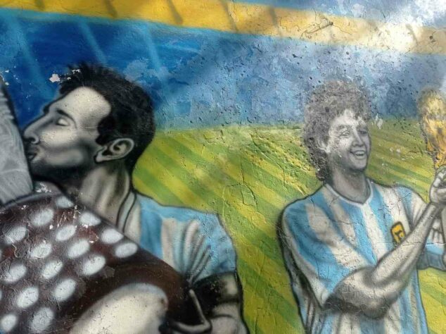 Retrato de Lionel Messi, com a taça da Copa América de 2021, conquistada contra o Brasil, ao lado de Maradona erguendo a Copa do Mundo de 1986.