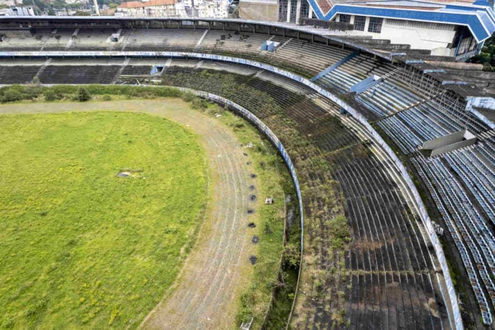 Na vista aérea, é possível ver o estádio tomado por mato nas arquibancadas e ao redor da pista de atletismo. 