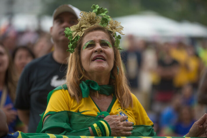 A plenos pulmões, uma torcedora canta o hino nacional a minutos da estreia: é jogo de Copa do Mundo! 