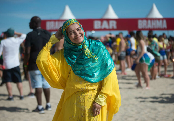 De verde e amarelo, uma torcedora aguarda sorridente pelo início da partida. 